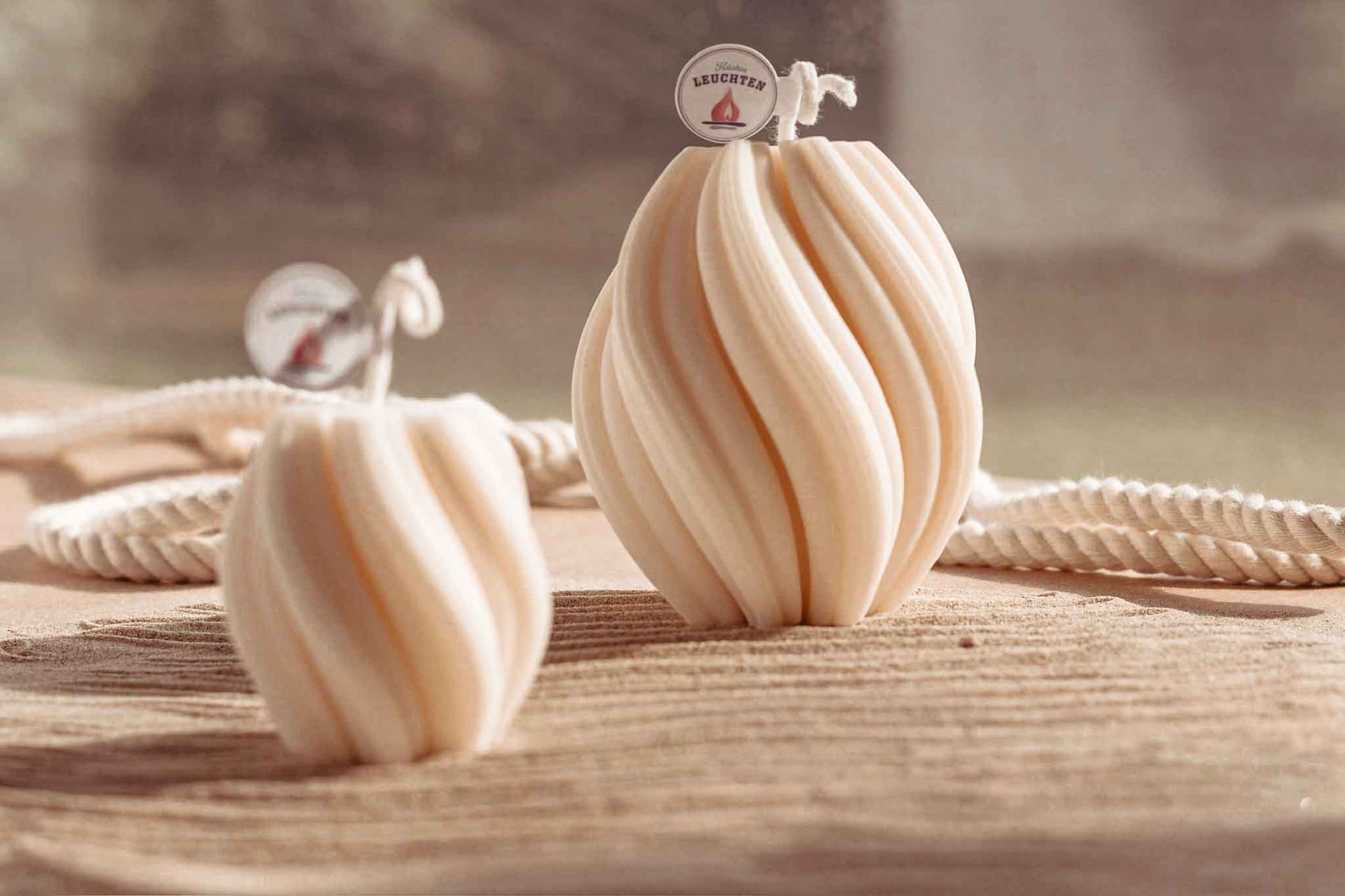 zwei gedrehte Rapswachskerzen auf Sand im Hintergrund weißes Seil