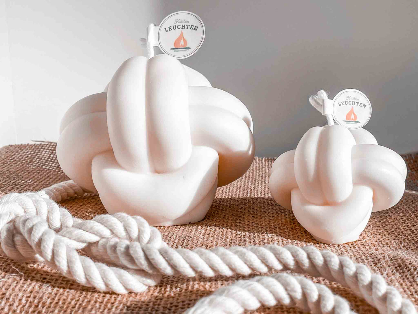 2 Knotenkerzen in groß und klein auf Jutestoff im Vordergrund Seil mit Achterknoten