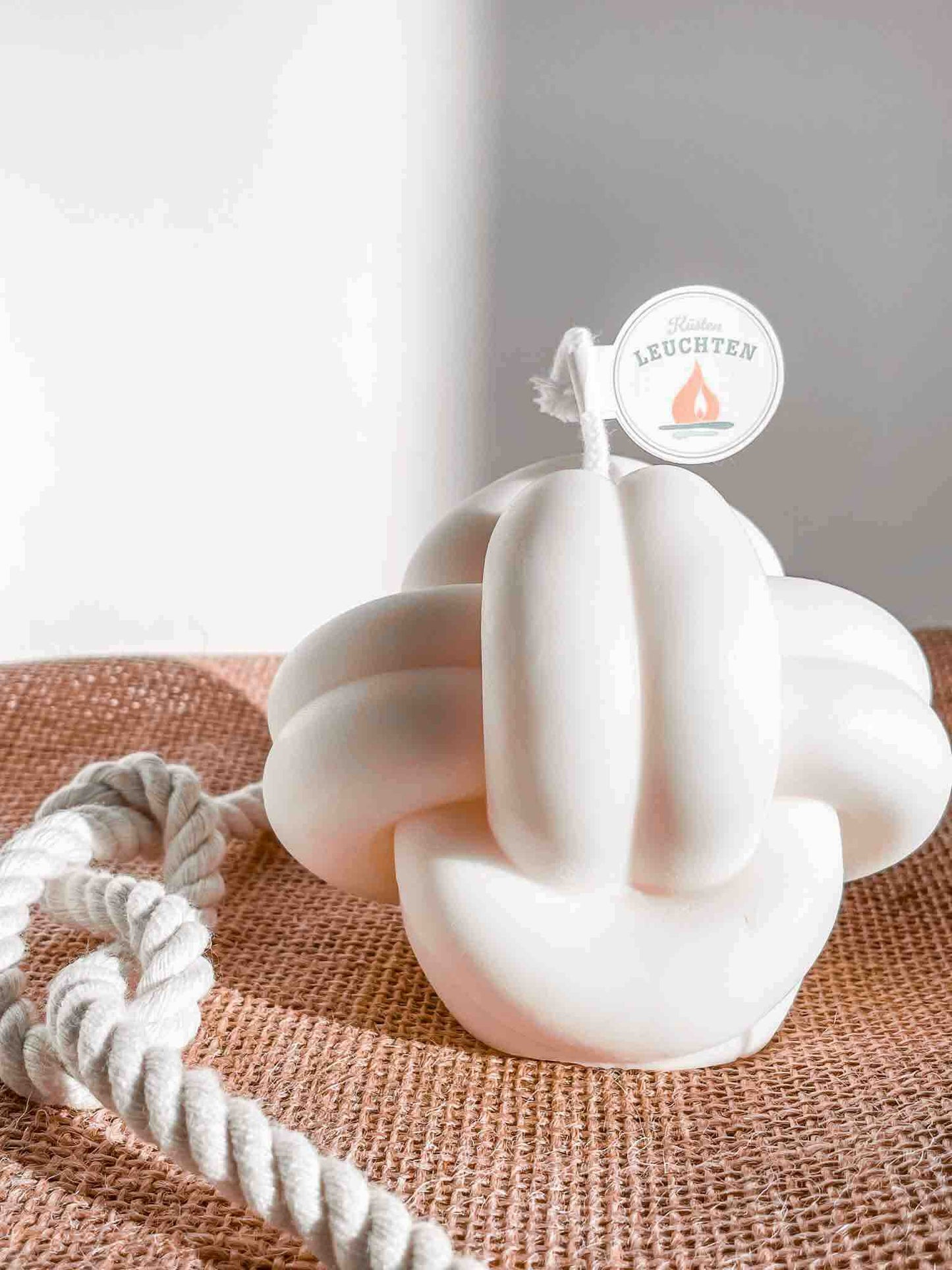 große cremeweiße Knotenkerze auf Jutestoff seitlich  weißes Seil mit Achterknoten