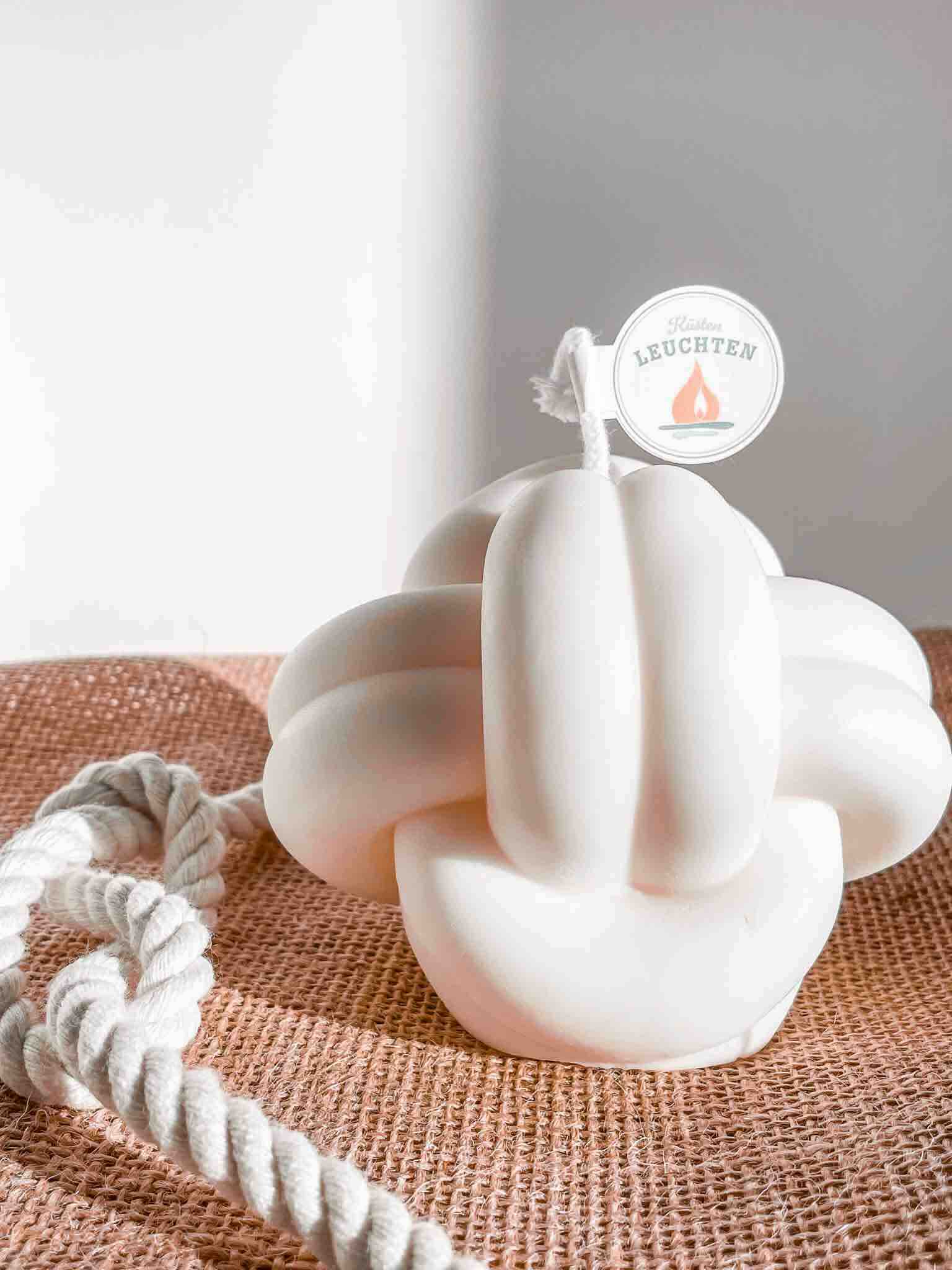 große cremeweiße Knotenkerze auf Jutestoff seitlich  weißes Seil mit Achterknoten