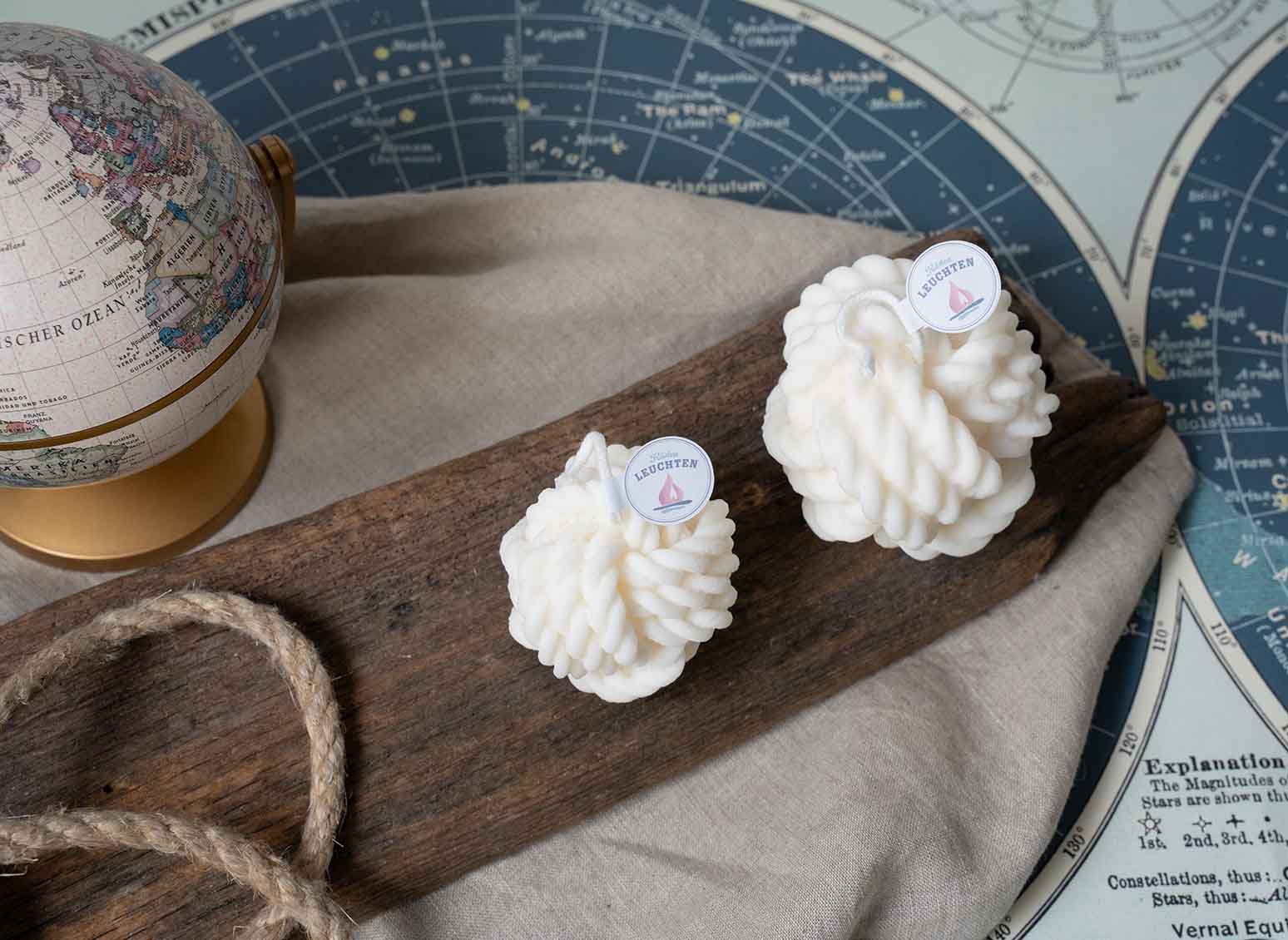 2 cremeweiße Tau Knoten Rapswachskerze auf Treibholz globus und Seekarte im Hintergrund