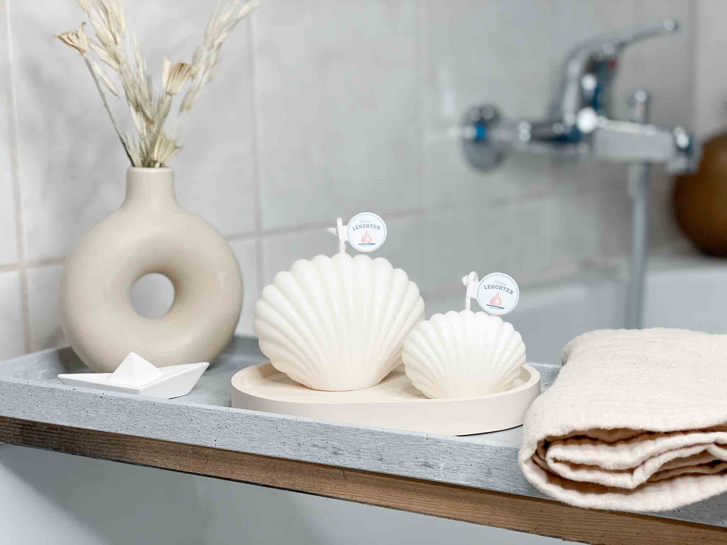 Muschelkerzen in groß und klein auf Badewannenablage kleines Schiffchen als Deko und Handtuch im rechten Vordergrund