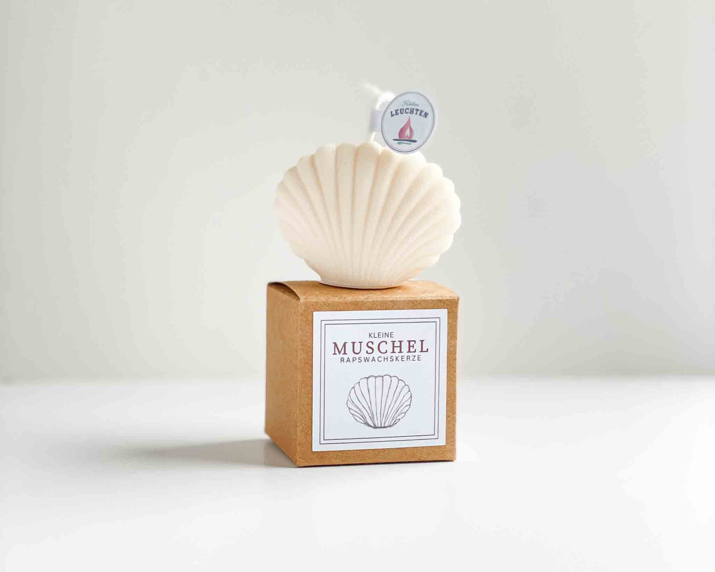 cremeweiße Muschel steht auf brauner Verpackung mit weißem Etikett