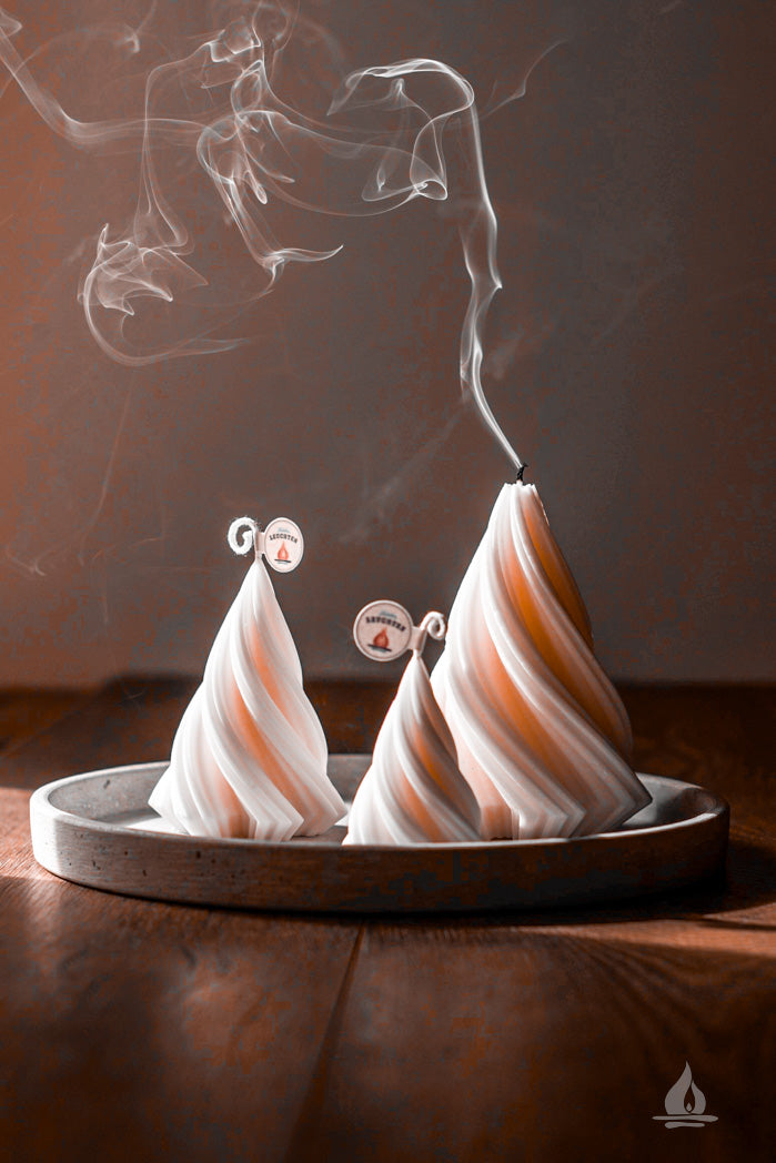 3 Kerzen als gedrehte Tannenbäume auf Betonschale mit aufsteigendem Rauch