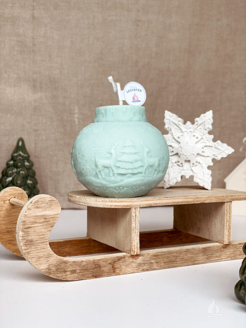 Weihnachtskugel Rentier eisblau auf Minitatur-Schlitten im Hintergrund kleine Deko-Tanne