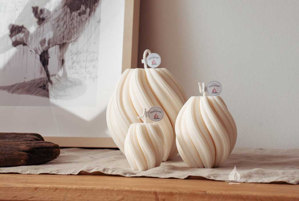 3 unterschiedliche große gedrehte Rapswachskerzen auf Sideboard Bilderrahmen im Hintergrund