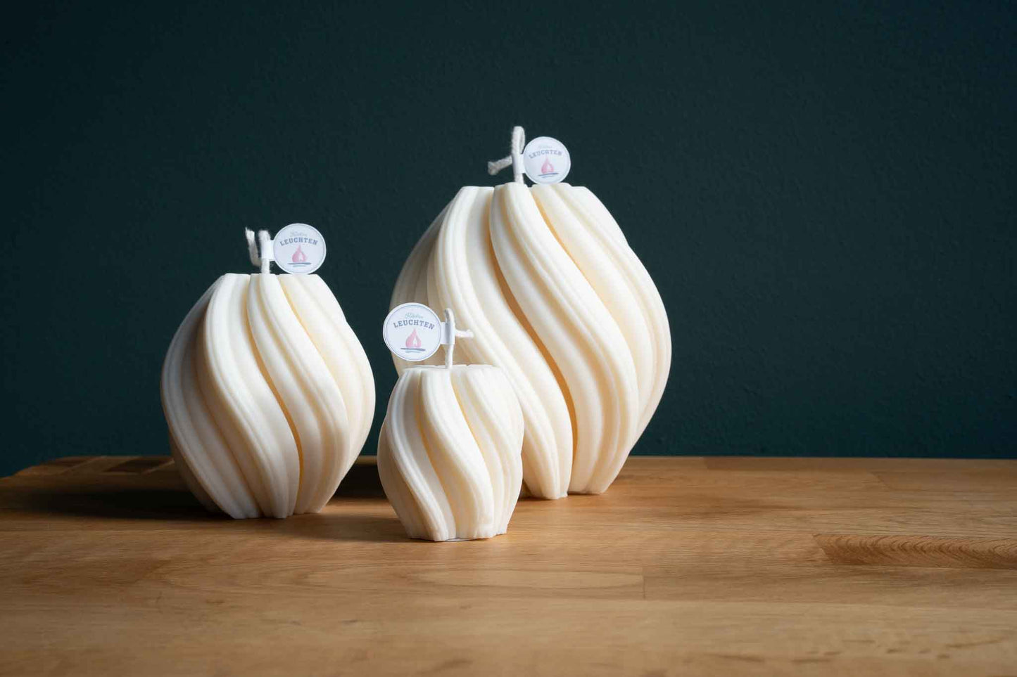 3 Größen Wellenkerze in cremeweiß auf Holztisch mit dunkelgrünem Hintergrund