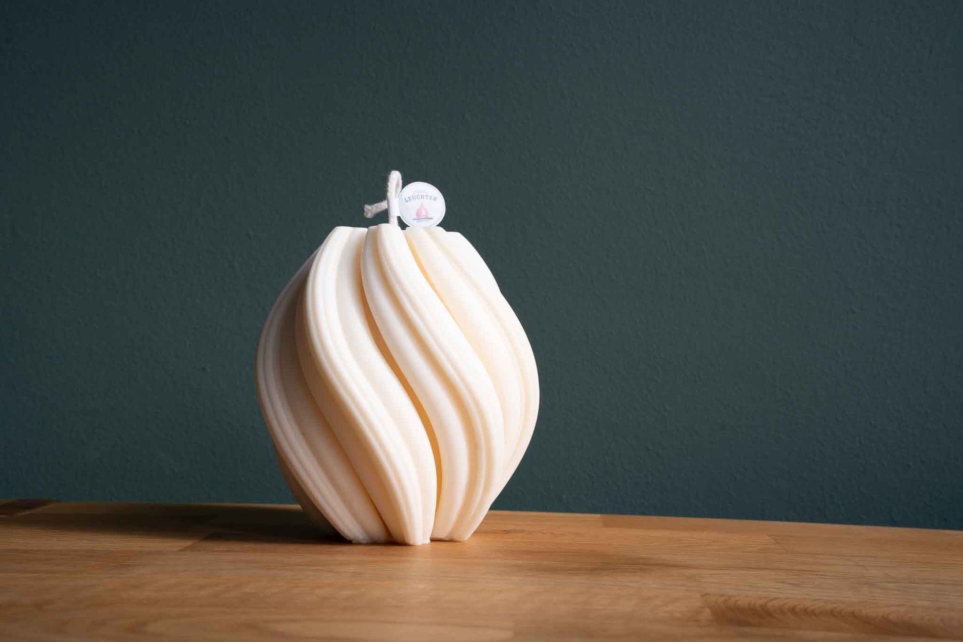 große cremeweiße Wellenkerze auf Holztisch vor dunkelgrünem Hintergrund