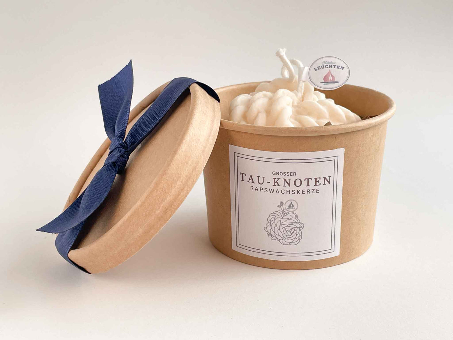 Tau-Knoten-Kerze in brauner Verpackung Deckel aufgestellt mit blauer Schleife
