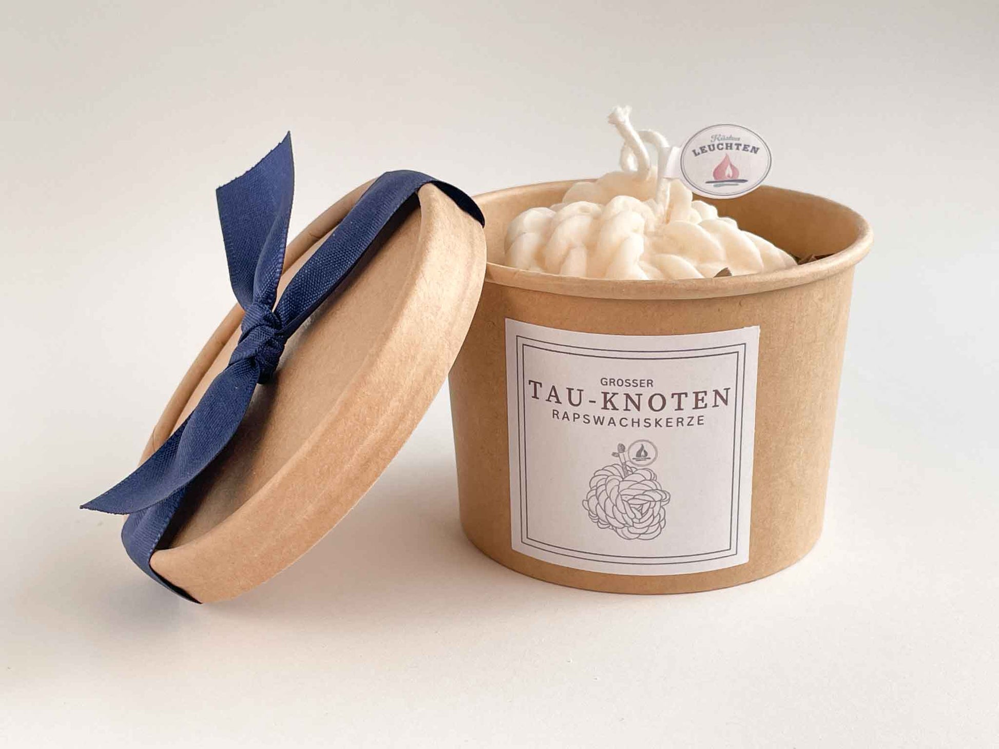 Tau-Knoten-Kerze in brauner Verpackung Deckel aufgestellt mit blauer Schleife