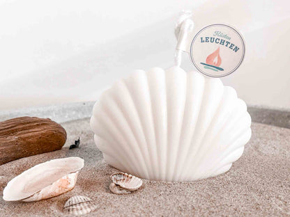kleine Muschelkerze in cremeweiß auf Strandsand Strandgut im linken VOrdergrund 