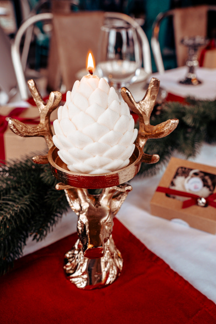 detailreiche weiße Tannenzapfenkerze auf einem goldenen Kerzenständer in Hirschform
