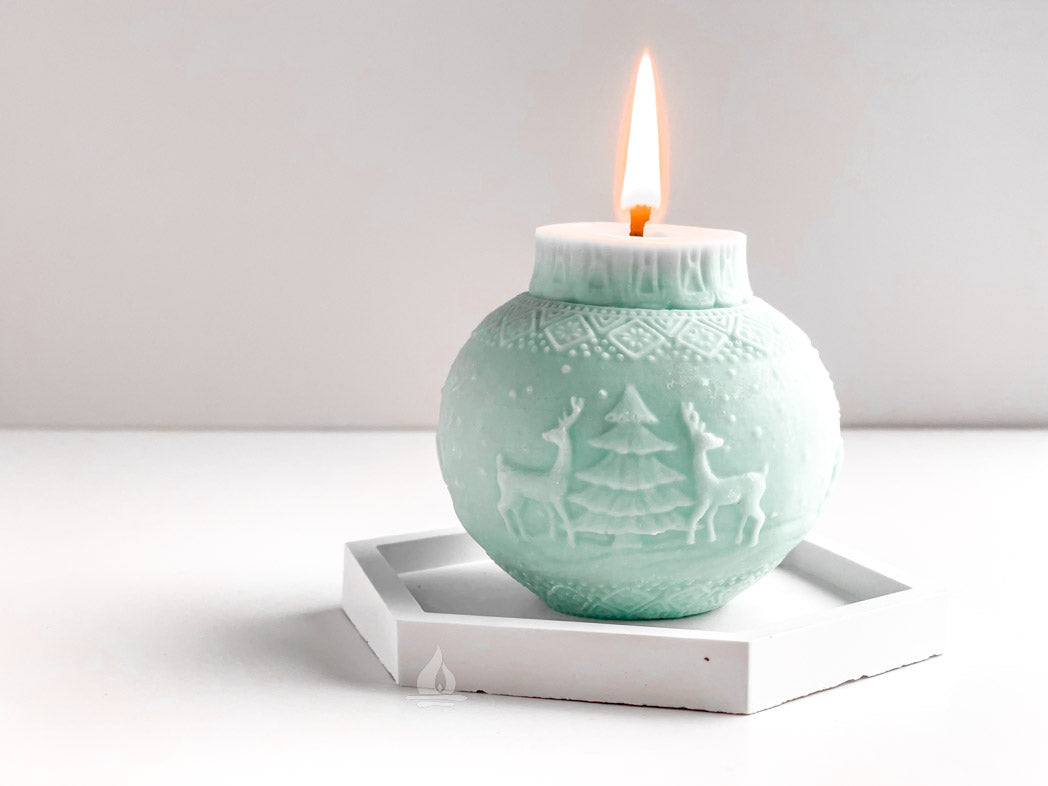 brennende Rapskerze in Kugelform mit Rentiermotiv in eisblau auf sechseckigem Tablett