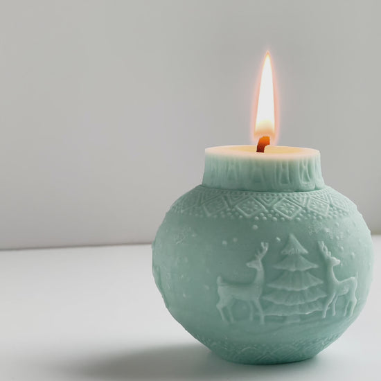 brennende Kugelkerze in eisblau mit Motiv mit zwei Rentiere und einem Tannenbaum