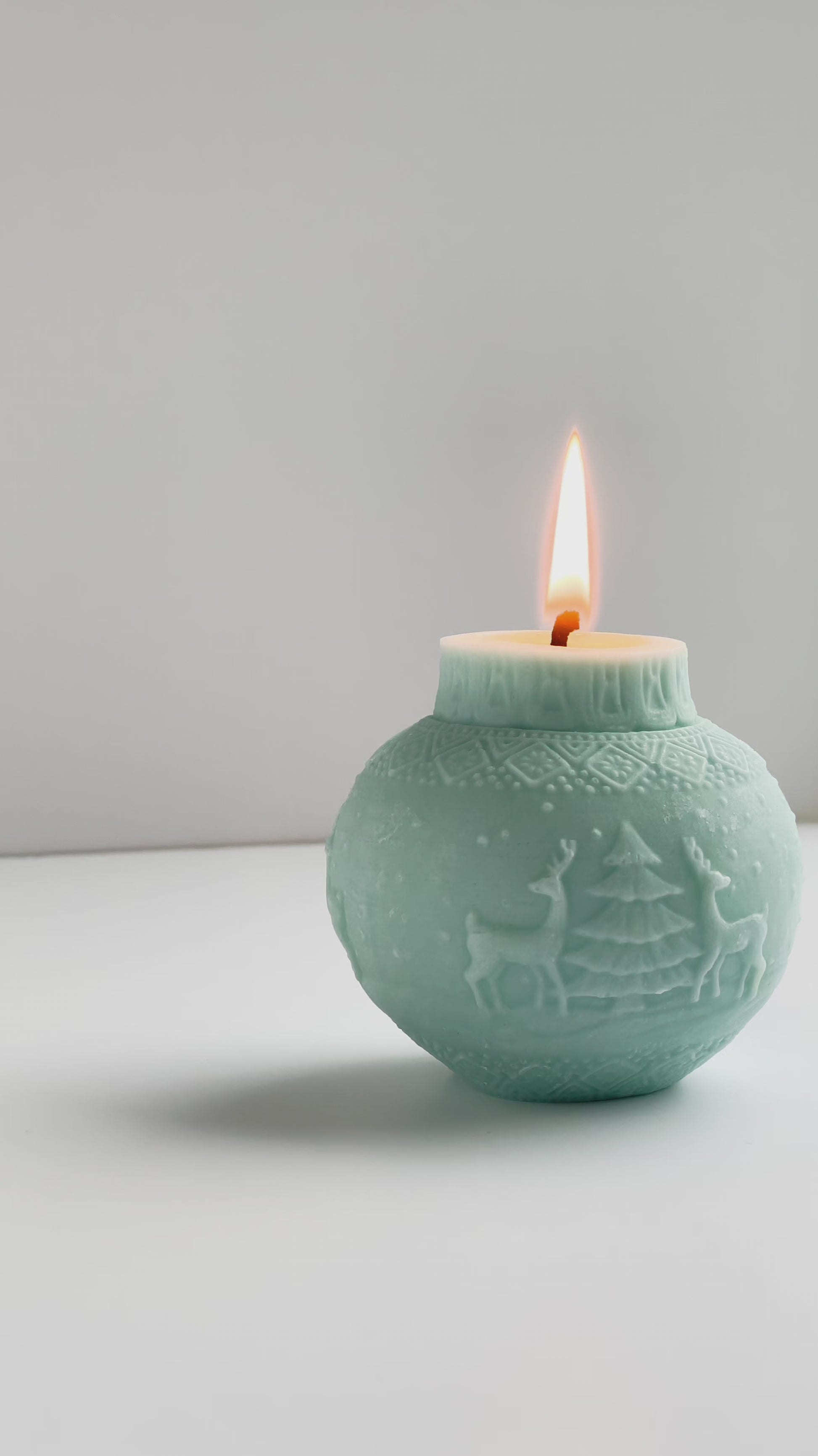 brennende Kugelkerze in eisblau mit Motiv mit zwei Rentiere und einem Tannenbaum